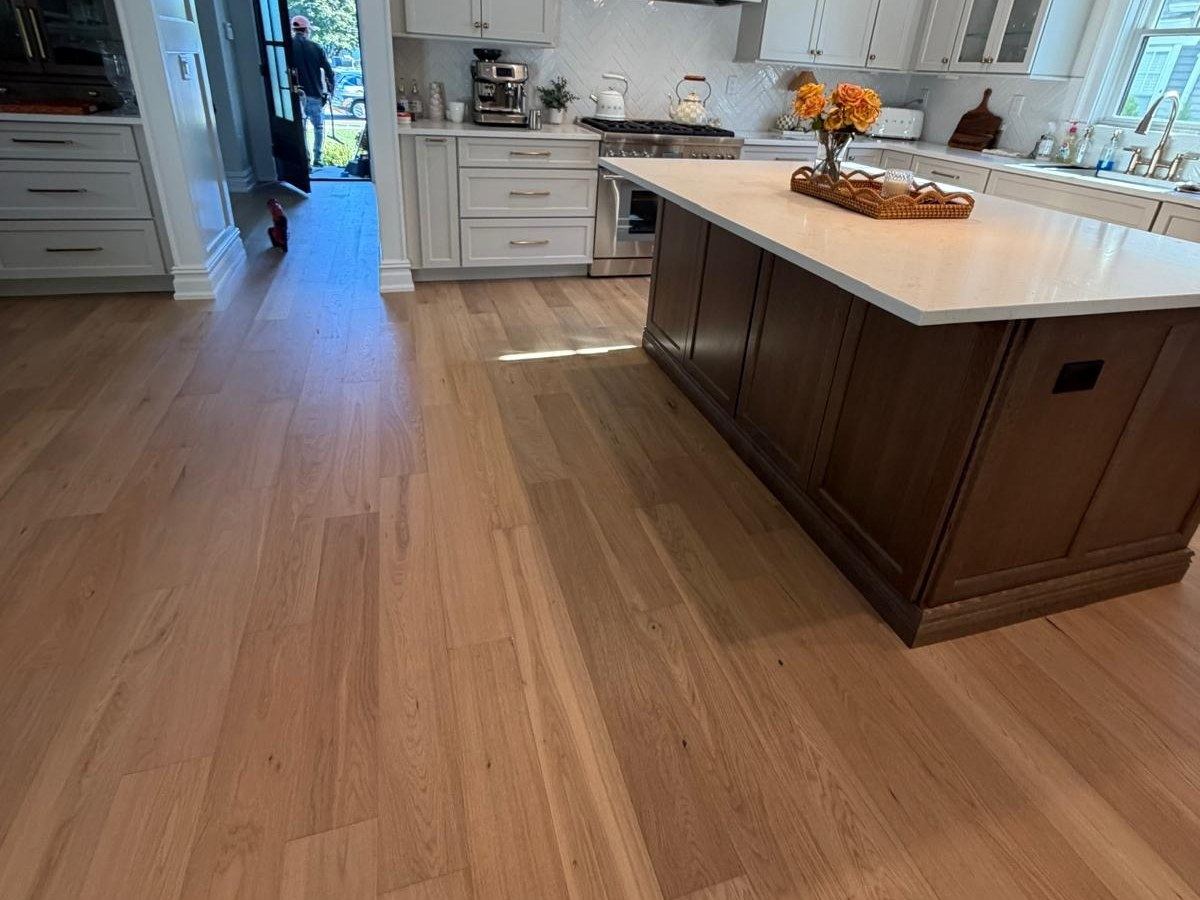 Hardwood floor running through a kitchen past a dark wood island